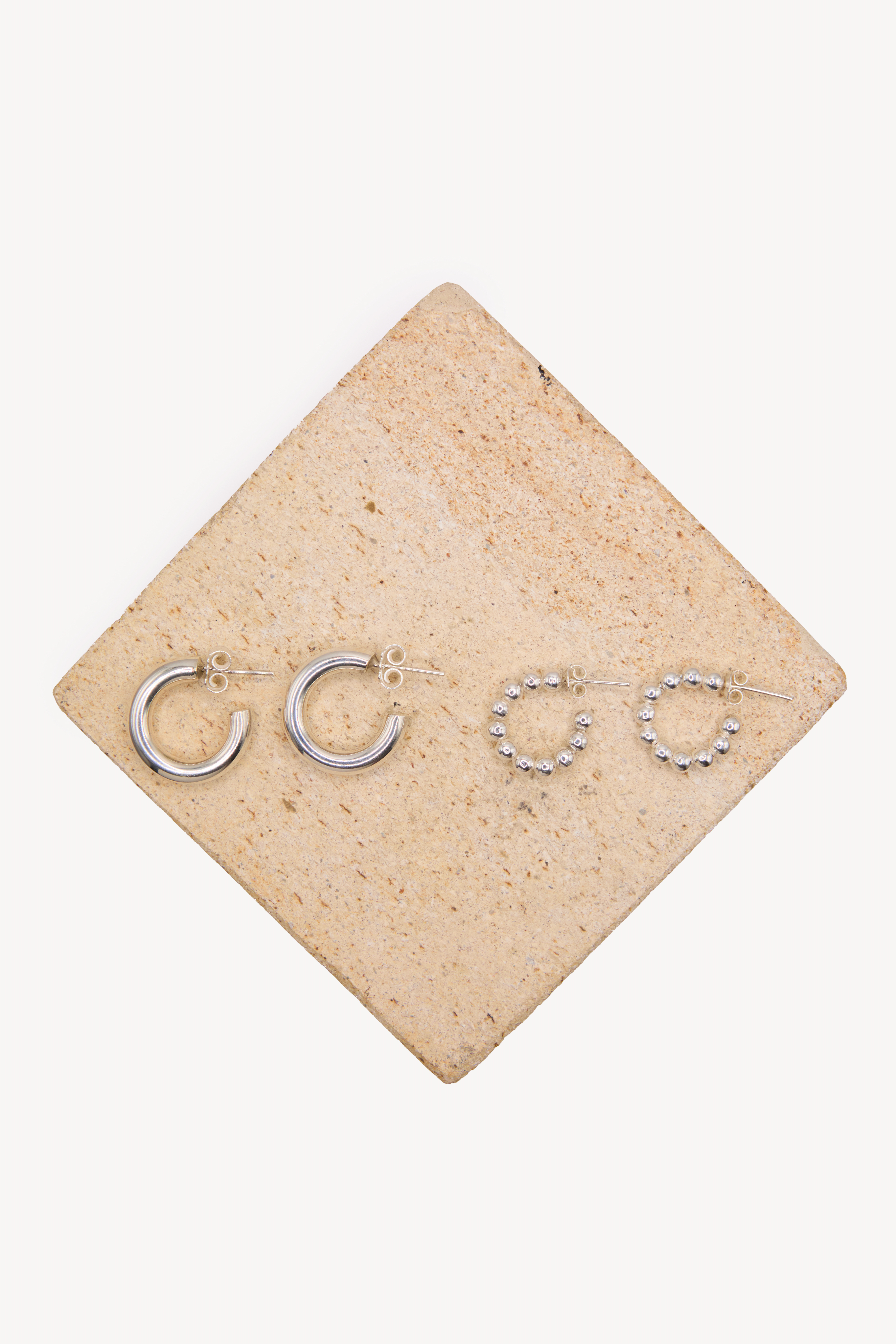 Two pairs of handmade earrings on a box with a neutral background