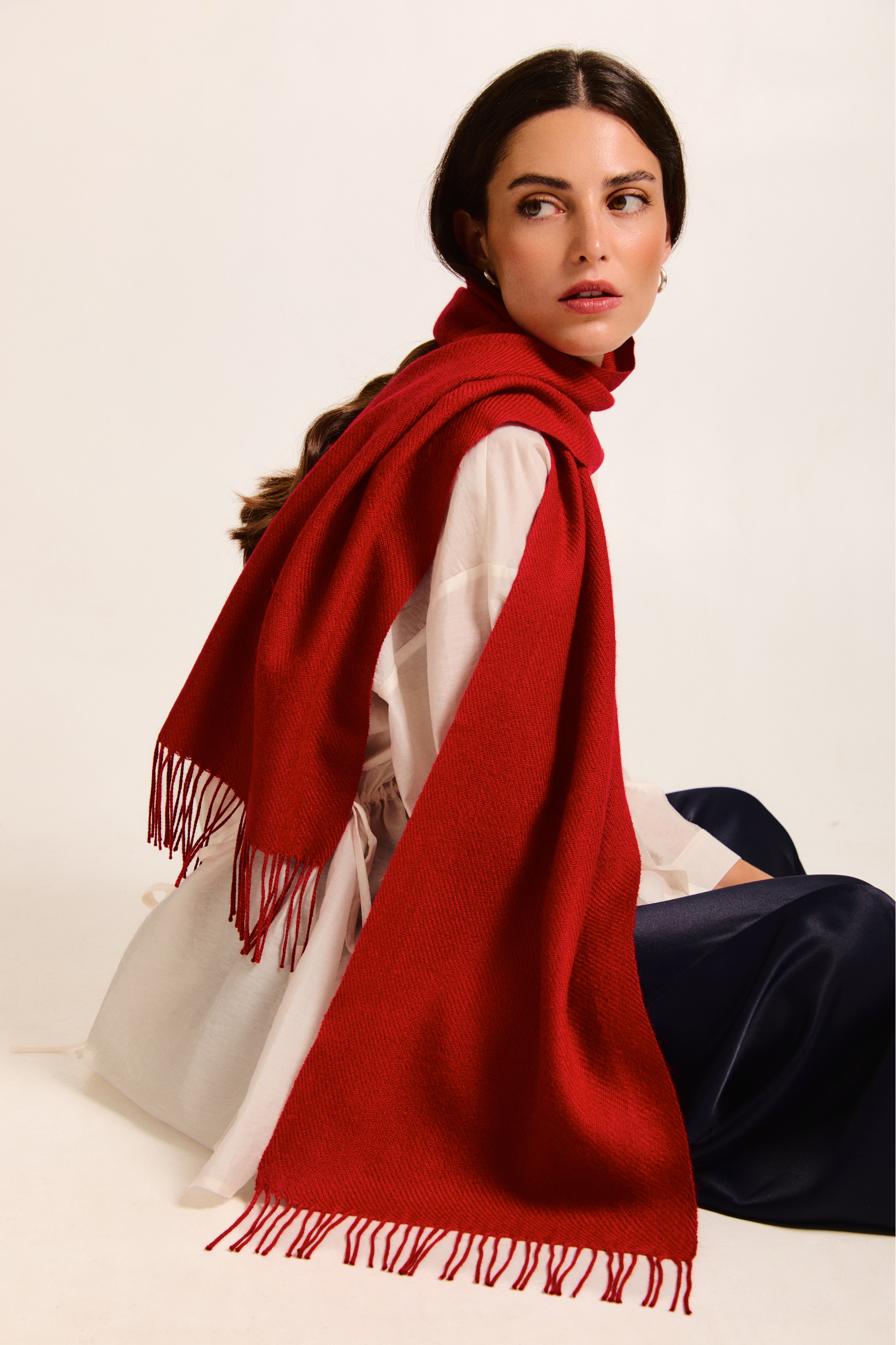 Model sitting with a red handmade scarf on a neutral background.